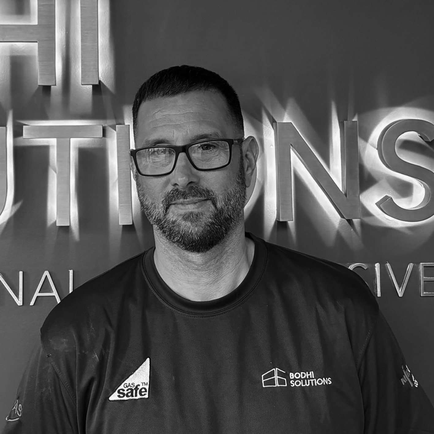 Man with glasses and beard wearing Bodhi Solutions shirt against company logo backdrop.