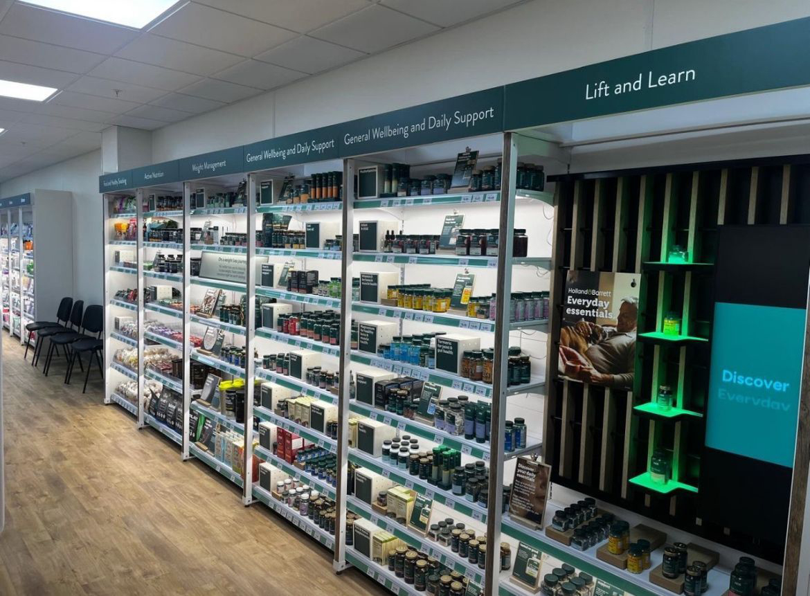 Pharmacy aisle with shelves stocked with supplement bottles under signs for wellness, weight, and daily support.