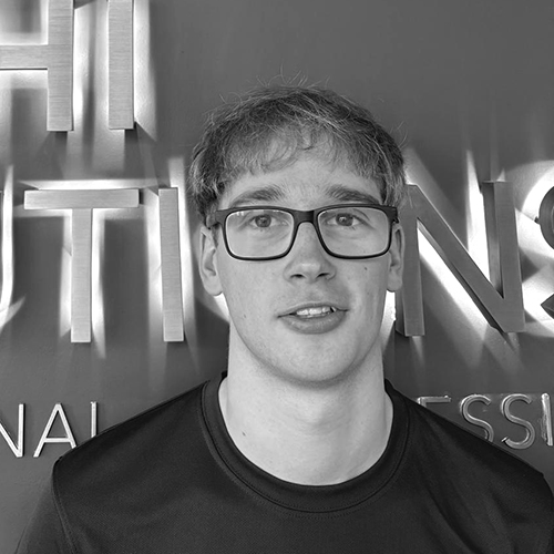 Young man with glasses and short hair wearing a dark shirt standing in front of a wall with large illuminated letters.