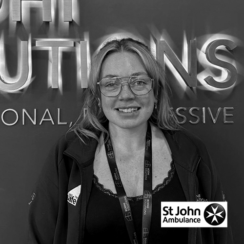 Smiling woman with glasses and lanyard stands in front of a wall with large text.