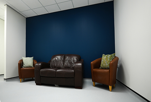 Two brown armchairs and a dark brown leather loveseat against a navy blue and white wall.