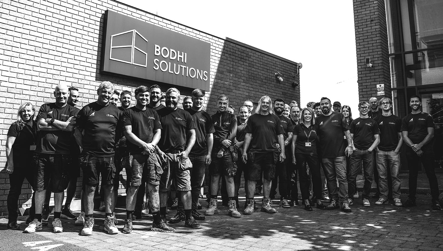 Group of Bodhi Solutions employees posing outside the company building under company sign.