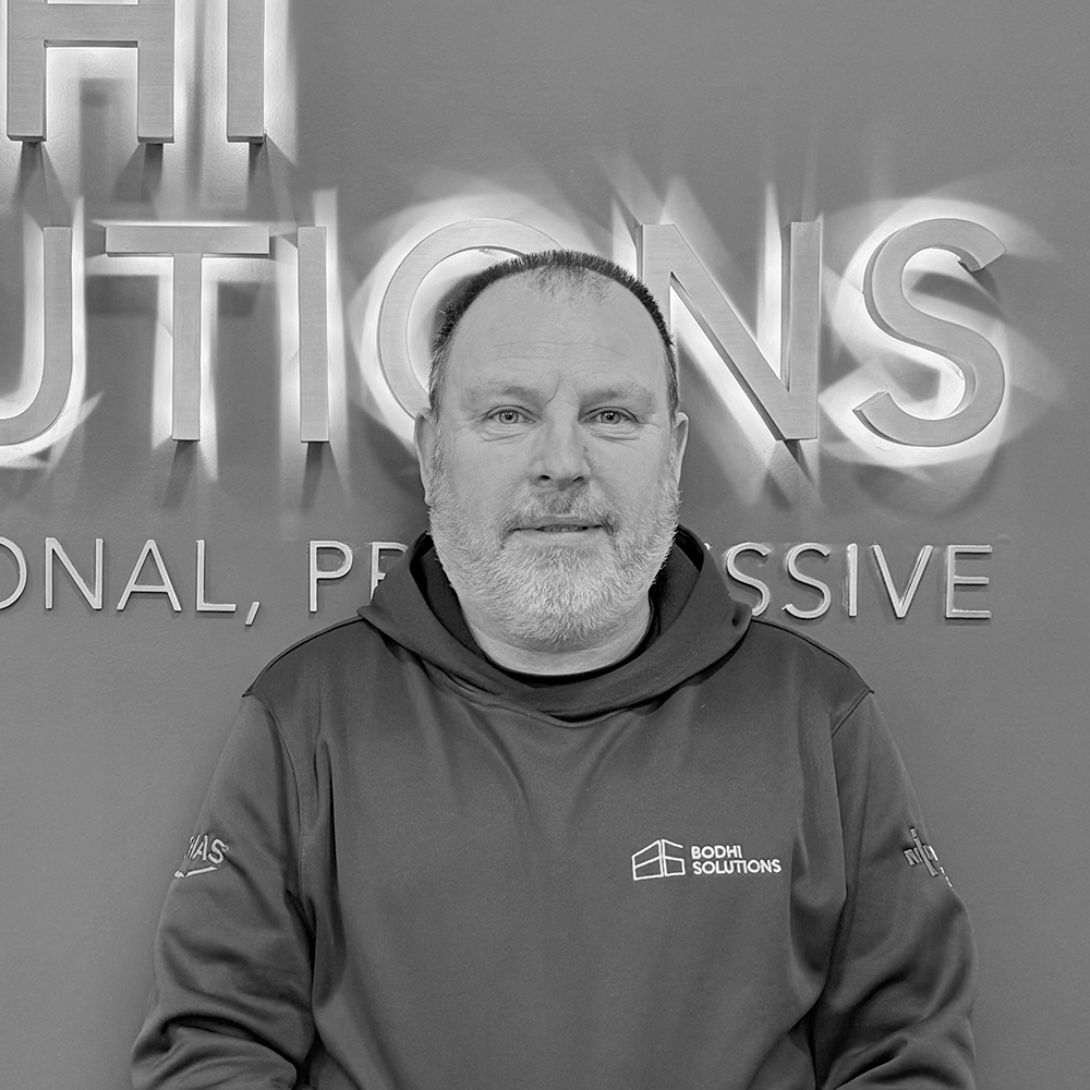 Man with short hair and beard wearing Bodhi Solutions hoodie standing against company sign.