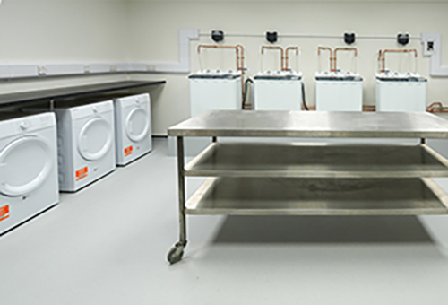 Laundry room with four washing machines, four dryers, and a metal folding table on wheels.