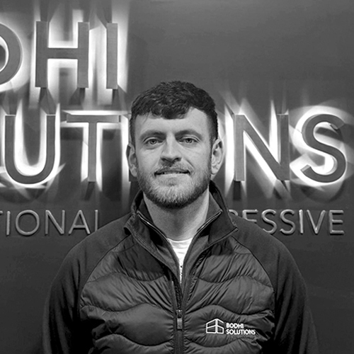 Man with short hair and beard wearing a Bodhi Solutions jacket standing in front of a Bodhi Solutions sign.