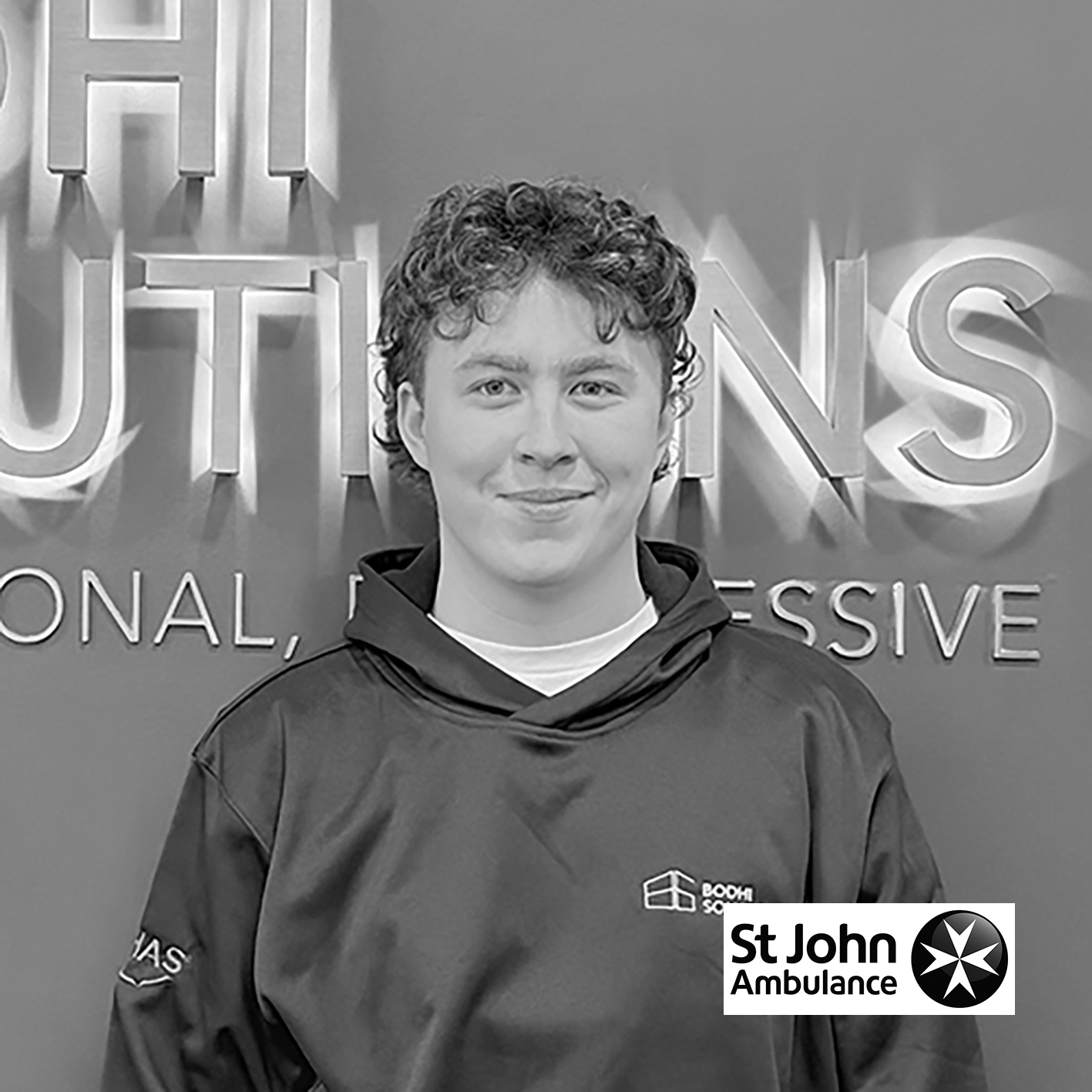 Smiling young man with curly hair wearing a Bodhi Solutions hoodie in front of company signage.