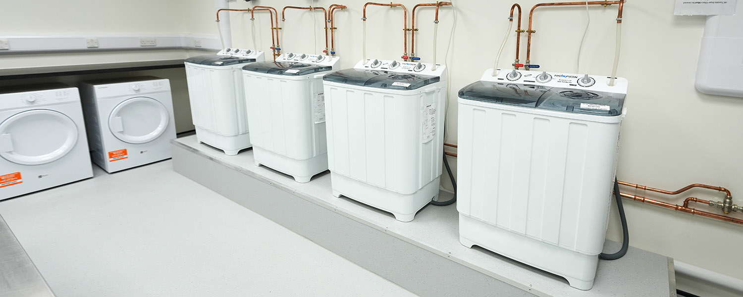 Clean laundry room with four top-load washing machines and two front-load dryers on white floor.