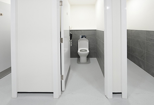 Modern public restroom stall with white toilet, gray tiled walls, and white partitions.