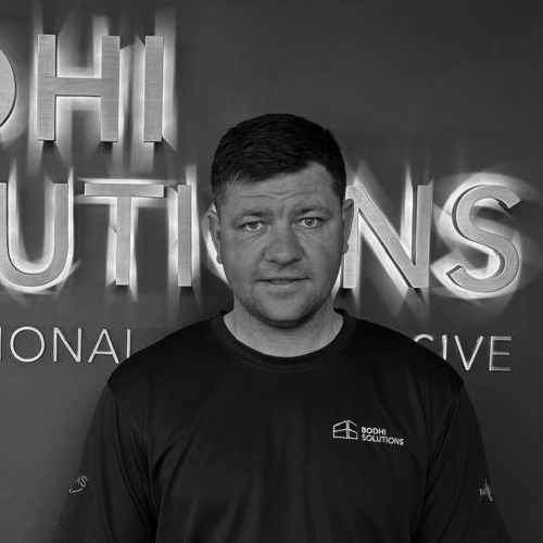 Man with short dark hair wearing a Bodhi Solutions shirt standing against a company logo wall.