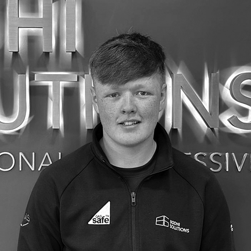 Young man with short hair and freckles wearing a Bodhi Solutions jacket standing in front of logo.