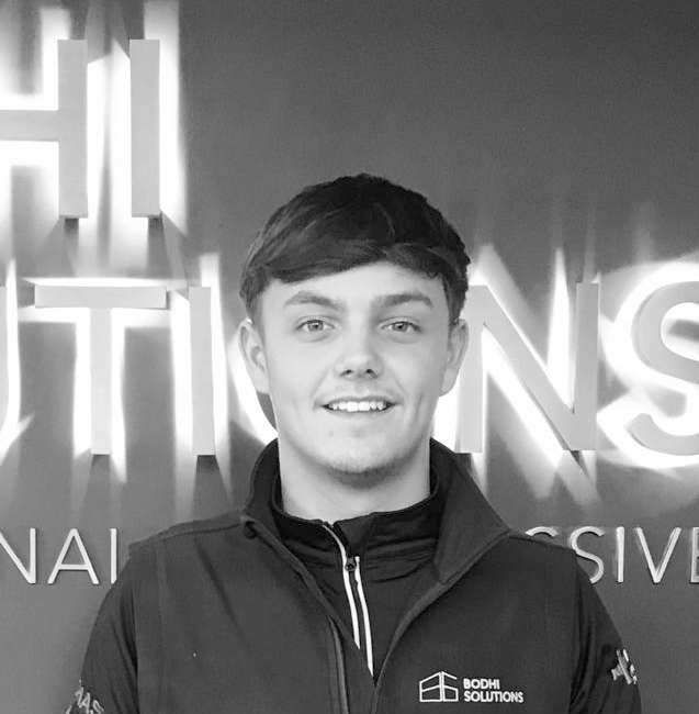 Young man in a Bodhi Solutions jacket smiling in front of a sign with glowing letters.