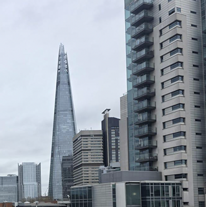 The Shard skyscraper among other buildings under a cloudy sky in a cityscape.
